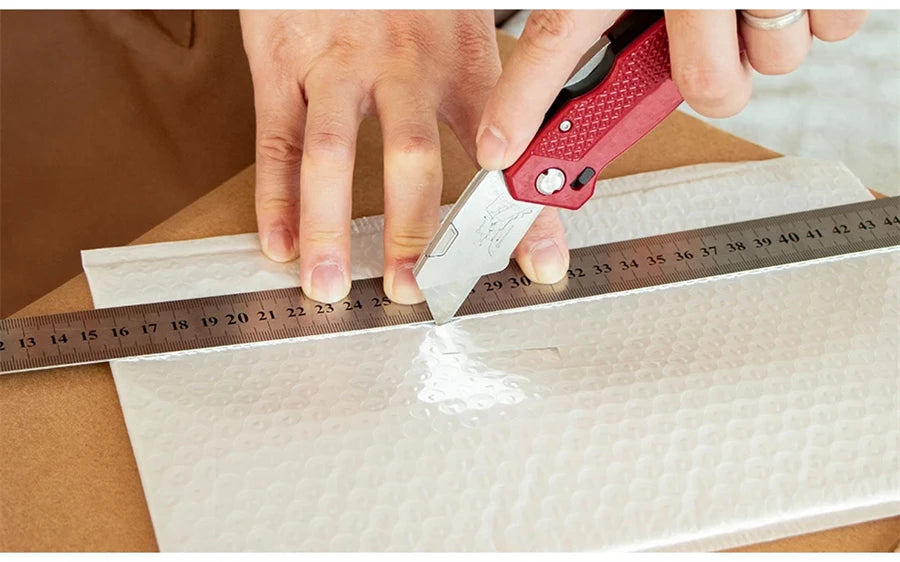 Folding Utility Knife - Red utility knife in use scoring sheet material along a straight edge ruler | Wrench Haus